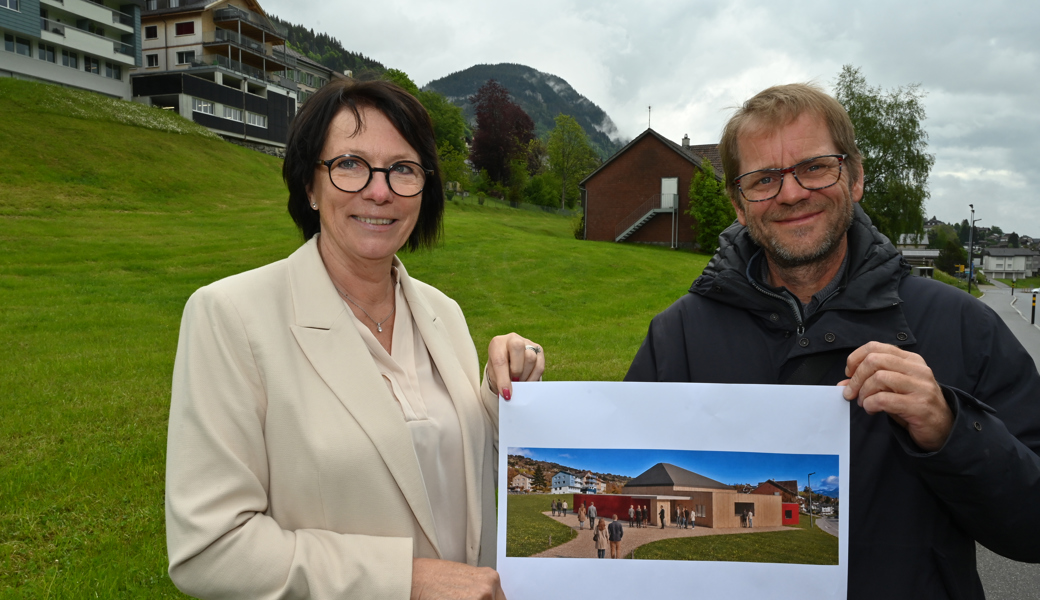 Katrin Frick und Martin Sailer mit einer Visualisierung vor der grünen Wiese, auf die der Neubau zu stehen kommen soll.