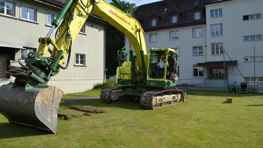 Baukommissionspräsident Beat Ernst bedient, unterstützt von Bauunternehmer Damian Oberhänsli, den Bagger für den Spatenstich.