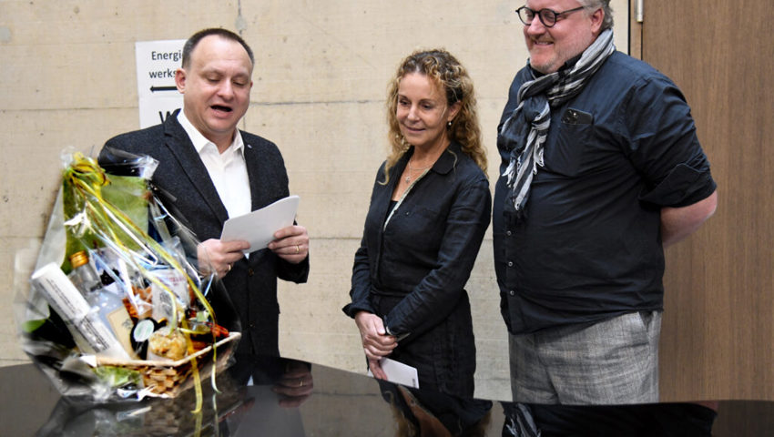  Gemeindepräsident Niklaus Lippuner (links) übergibt ein Geschenk an das Architektenteam Patricia Krebs und David Hofer.