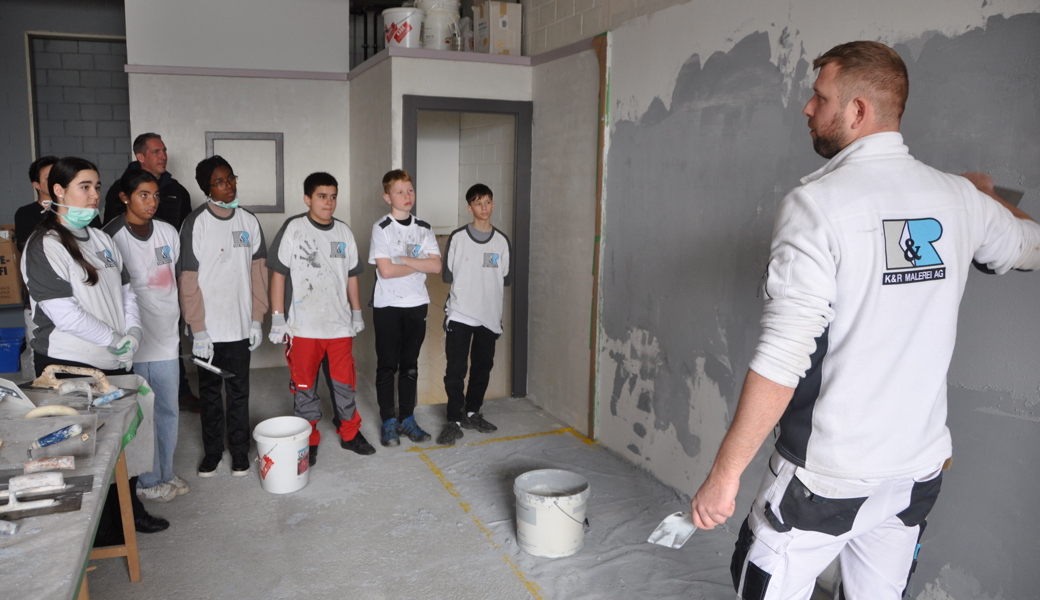 Der Firmenchef erklärt und zeigt vor, weshalb sein Beruf so kreativ sein kann: Cyrill Keller von der K&R-Malerei, aufmerksam verfolgt von Schülerinnen und Schüler sowie Michael Giger, Präsident des Gewerbevereins Sevelen.
